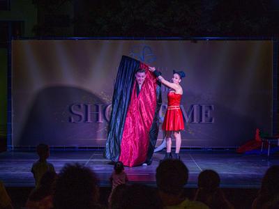 Un mago realiza un truco con un paño rojo y una caja en el escenario.
