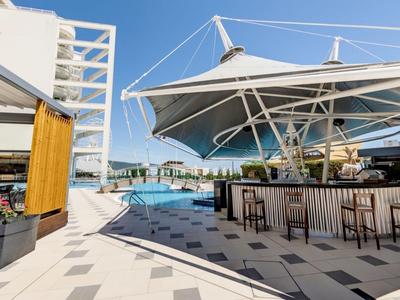 Piscina exterior moderna con bar y áreas de descanso bajo toldos blancos.