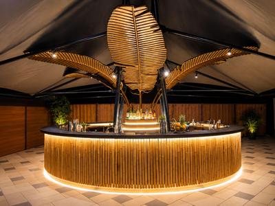 Modernes, rundes Bar-Setup mit warmem Licht und skulpturalen, goldfarbenen Blätterdekorationen.