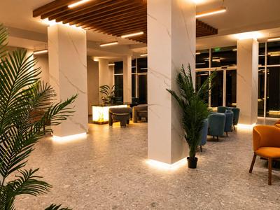 Heller Hotel-Loungebereich mit Marmorwänden, grünen Pflanzen und bunten Sitzmöbeln bei Nacht.