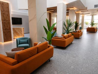Moderner Hotel-Lobby-Bereich mit orangenen Sofas, grauem Boden und grünen Pflanzen.