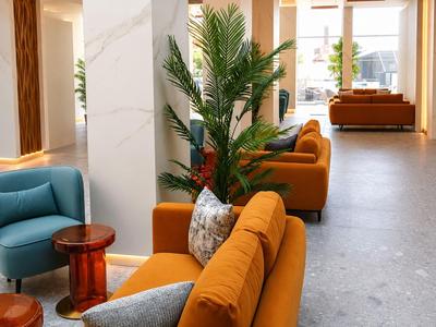 Moderne Hotellobby mit orangen Sofas, blauen Sesseln und grünen Pflanzen in hellem Raum.