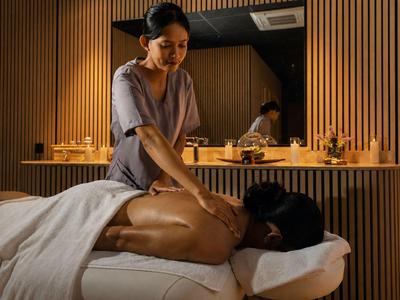 Terapeutka masuje plecy leżącej kobiety w przytulnie oświetlonym pokoju spa.