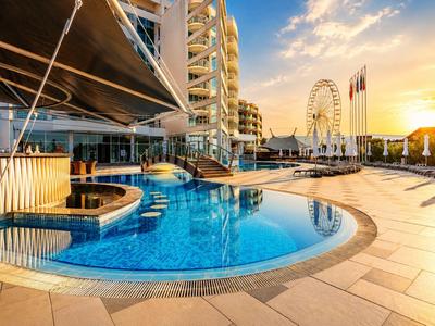 Nowoczesny kompleks hotelowy z basenem, tarasem słonecznym i diabelskim młynem o zachodzie słońca.