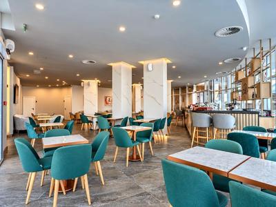 Nowoczesna sala jadalna hotelu z niebieskimi krzesłami i drewnianymi stołami, jasne wnętrze z dużymi oknami.
