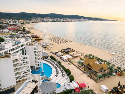 Widok na hotel z basenem obok długiej piaszczystej plaży i spokojnego morza o zachodzie słońca.