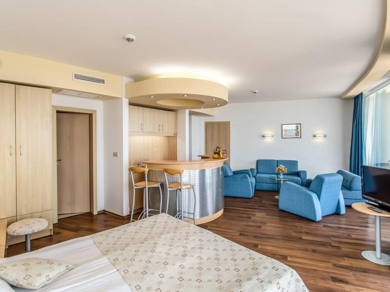 Ruime hotelkamer met bed, blauwe fauteuils, houten vloer en raam met gordijnen.