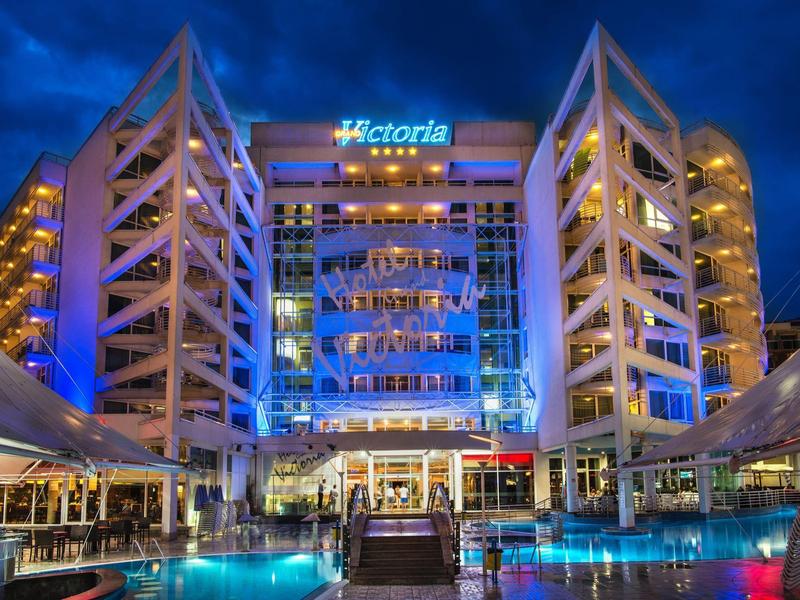 Modern hotel verlicht 's nachts met zwembad en loungegedeeltes voor een donkere blauwe lucht.