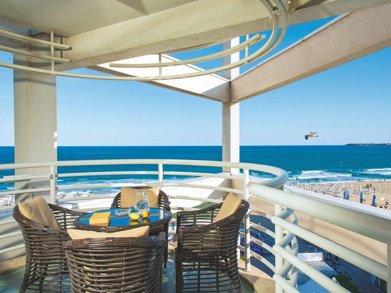 Balkon met eethoek met uitzicht op strand en oceaan onder een helderblauwe hemel.