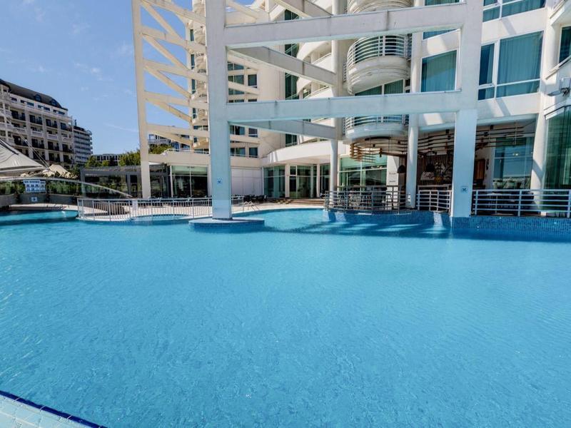 Leeg buitenzwembad van hotel met helder blauw water en witte parasols in de zon.