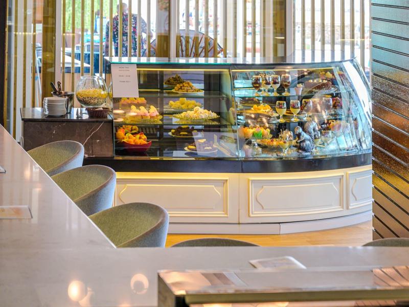 Moderne cafébalie met diverse gebakjes en desserts en zitgedeelte.