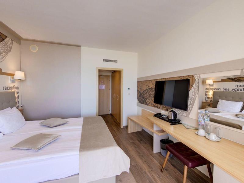 Lichte hotelkamer met twee bedden, een houten bureau en een grote spiegel.