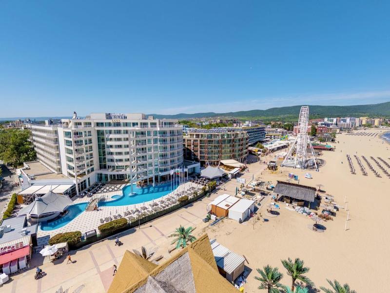 Breed strandzicht met hotels, ligstoelen en heldere lucht boven de zee.