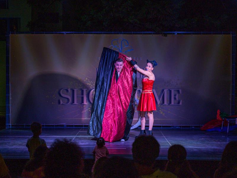 Een goochelaar in een rode jurk voert een illusie uit op het podium door een rode doek uit een zwarte doos te trekken.