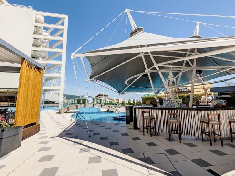 Moderne buitenzwembad met zonnescherm, barkrukken en uitzicht op zee bij een hotel.