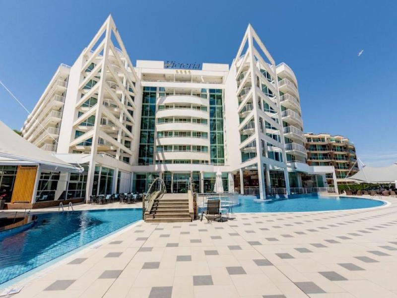 Modern hotelcomplex met groot zwembad en zonneterras onder een heldere blauwe lucht.