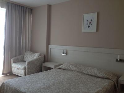 Simply furnished hotel room with double bed, armchair, and large window with curtains.