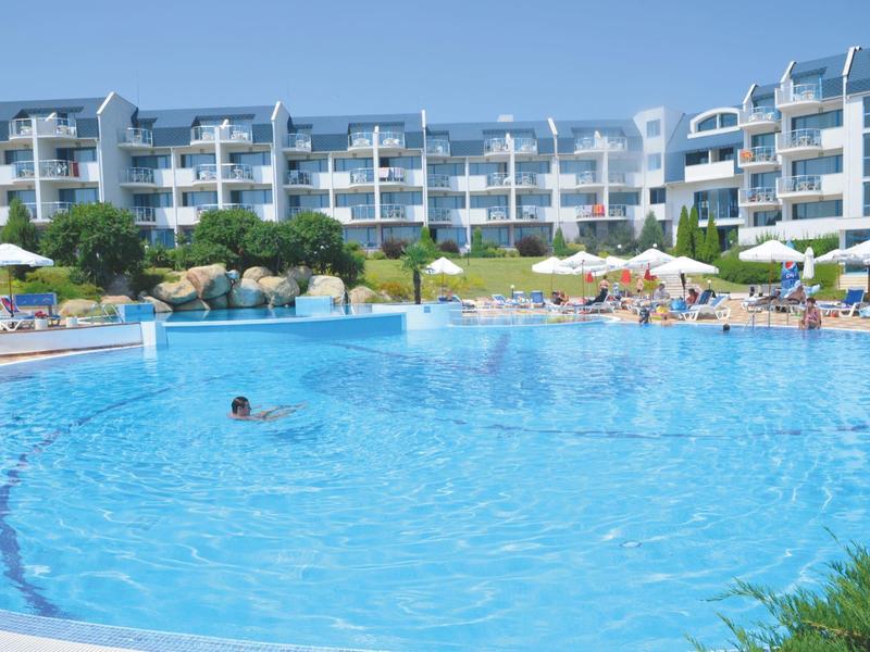 Large round hotel pool with sun umbrellas and multi-story hotel building in the background.