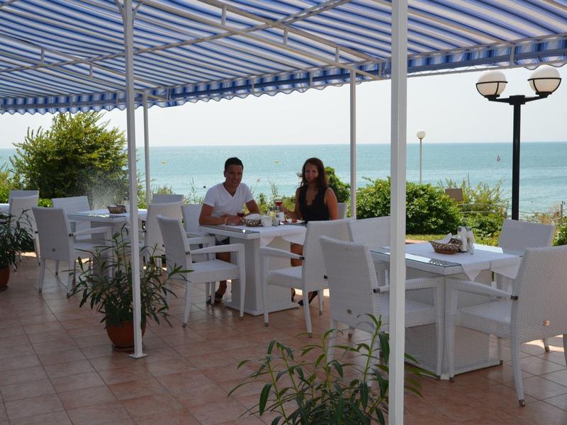 Terrace with white tables and chairs, sea view, two people dining.