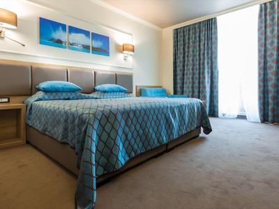 Modern hotel room with double bed, blue bedspreads, and large window with curtains.