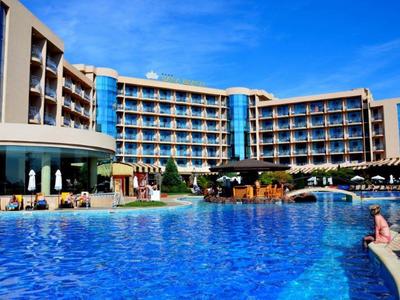 Modern hotel with large outdoor pool and sun terrace under clear blue sky.
