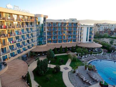 Large hotel with blue-tinted windows, garden area, and circular pool with sun loungers.