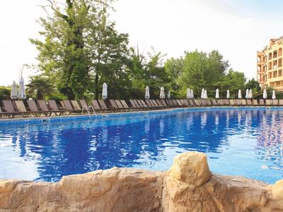 Großer Außenpool mit Liegestühlen und Bäumen im Hintergrund bei Sonnenschein.