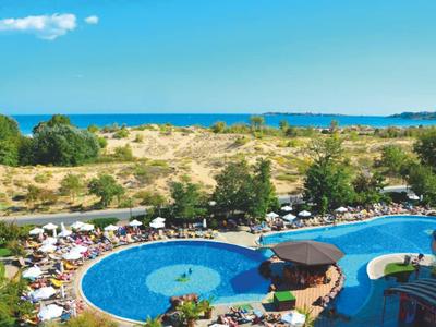 Large pool with sun umbrellas in front of a dune landscape by the sea.