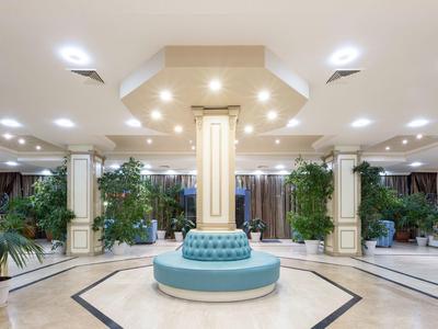 Elegant hotel lobby with round blue sofa and columns, decorated with plants.