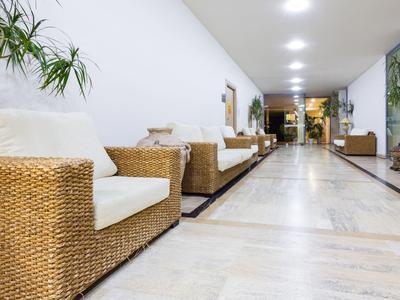 Long hotel corridor with rattan armchairs and white cushions on the left side.