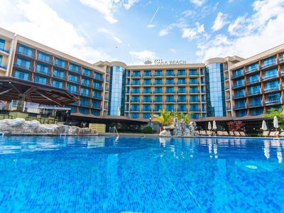 Large multi-story hotel with a spacious outdoor pool under a blue sky