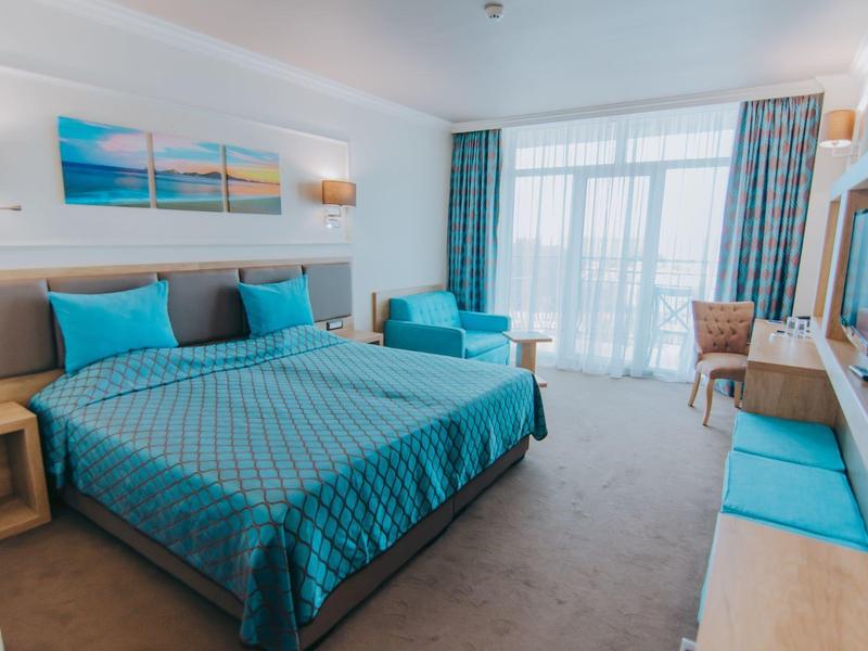 Bright hotel room with large bed, seating area, and balcony