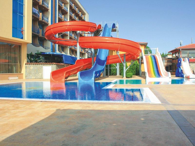 Colorful water slides by a hotel pool under clear blue sky.