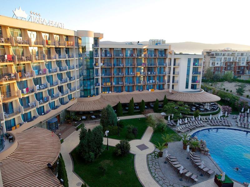 Large hotel with blue-tinted windows, garden area, and circular pool with sun loungers.