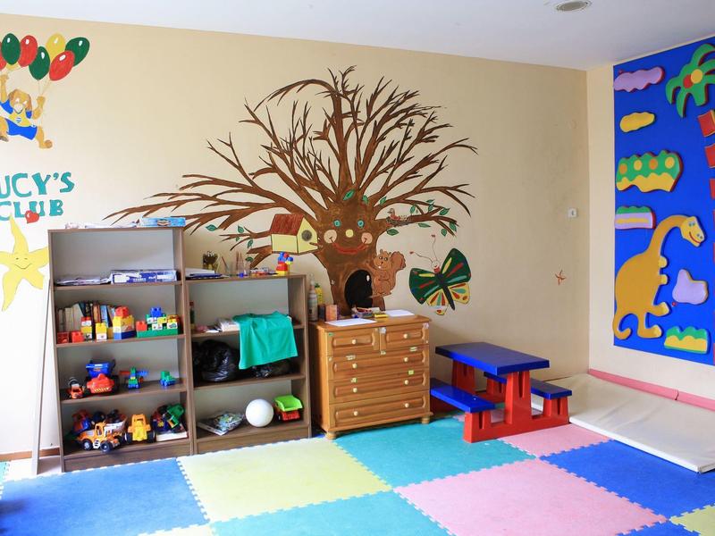 Colorful children's playroom with tree wall decoration, toy shelves, and padded floor mats.