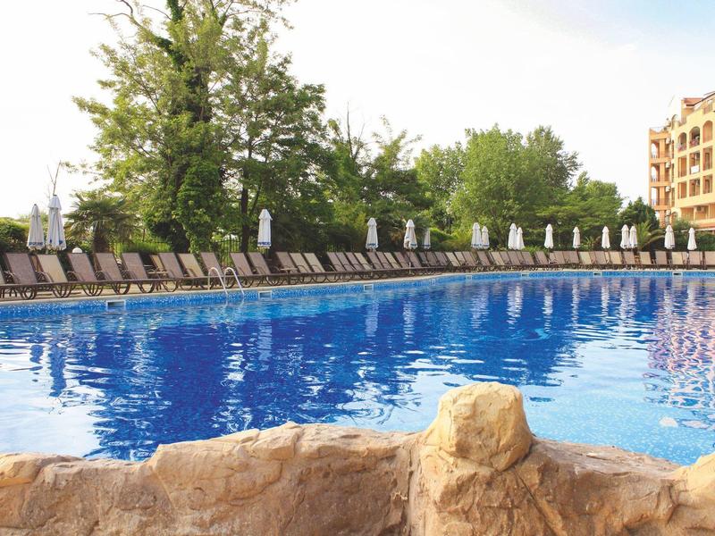 Large swimming pool with lounge chairs and umbrellas next to a hotel.