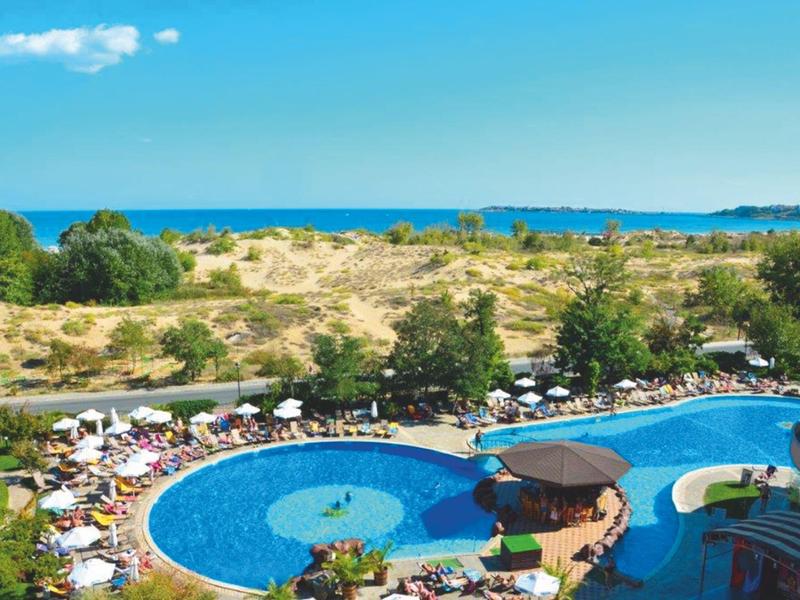 Large pool with sun umbrellas in front of a dune landscape by the sea.