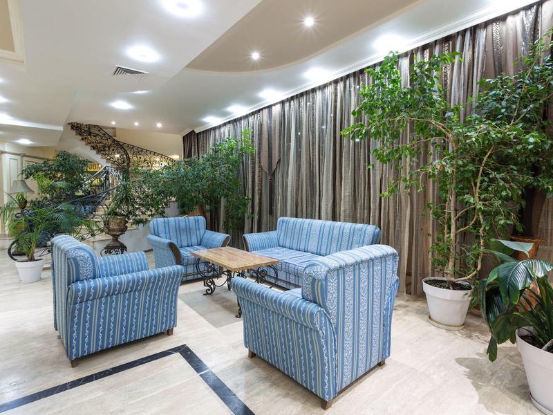 Cozy hotel lounge area with blue armchairs, sofa, plants, and curtains.