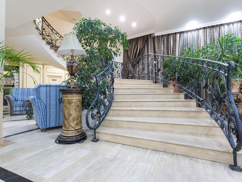 Elegant hotel lobby with curved marble staircase and green plants.