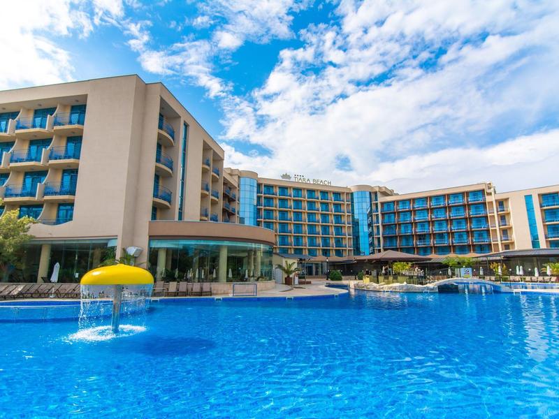 Large hotel with multi-story buildings and a big blue pool under a partly cloudy sky.