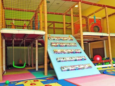 Kleurrijke indoor speelruimte voor kinderen met klimwand, schommel, netgaten en zachte vloerbedekking.
