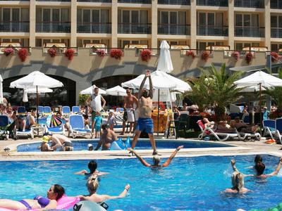 Menschen entspannen und spielen im Hotelpool, umgeben von Liegestühlen und Sonnenschirmen.