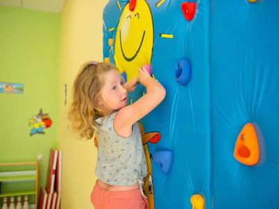 Jong meisje klimt op kleurrijke indoor klimwand met een glimlachend gezicht in een lichte kamer.