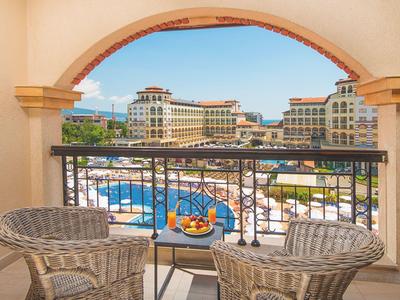 Balkon mit zwei Stühlen und Obstschale, Blick auf Hotelpool und mediterrane Gebäude.