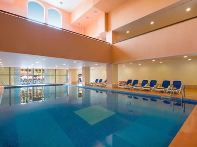 Overdekt zwembad met ligstoelen onder grote ramen in een ruime hotelruimte.