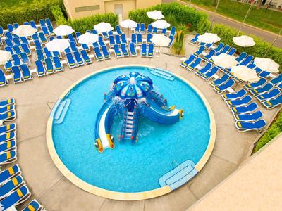 Rond zwembad met blauwe glijbaan en veel blauwe ligstoelen met witte parasols eromheen.