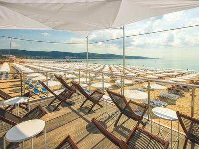 Strandparasolletjes en ligstoelen op een zandstrand aan zee onder een deels bewolkte hemel.