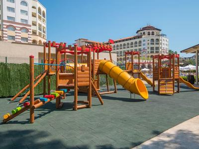 Buitenspeeltuin met glijbanen en klimtoestellen bij hotelgebouwen onder een heldere lucht.
