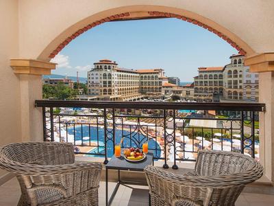 Uitzicht op een hotelzwembad en gebouwen vanaf een balkon met een tafel en twee stoelen.