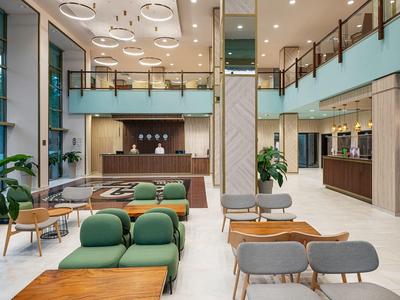 Ruime hotel lobby met moderne zitplaatsen, houten tafels en een receptiebalie onder helder licht.